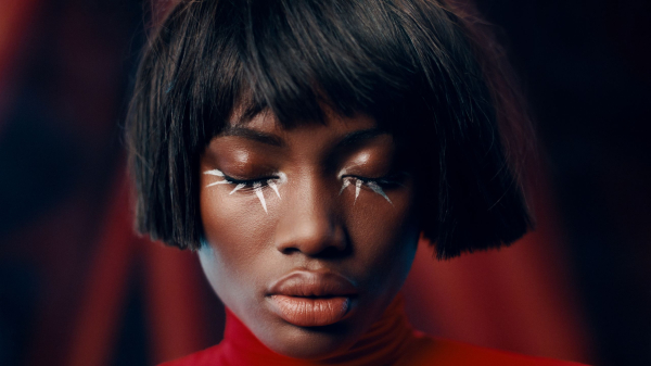 Image contains a model with white eyeliner on a dark red background