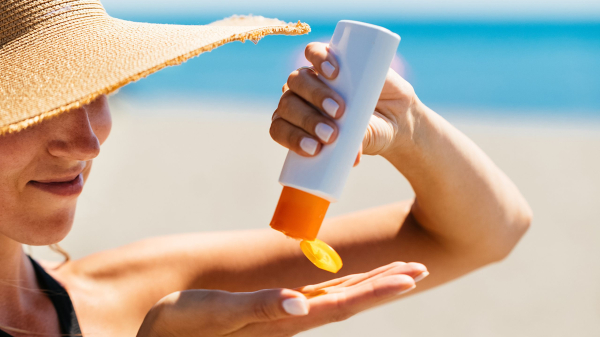 woman on the beach squirting sunscreen from a bottle onto her right hand