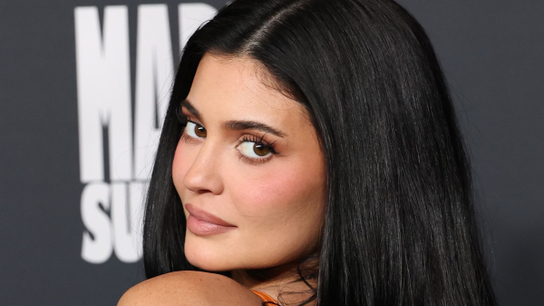 Kylie Jenner appears at the Marty Supreme premiere in an orange dress. She wears her hair down.